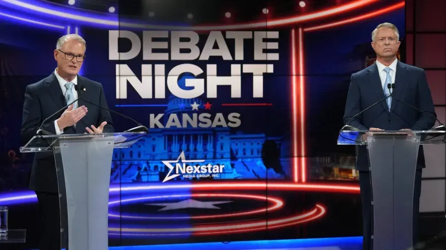 Two men stand at podiums on a set reading Debate Night Kansas, with Nexstar branding.