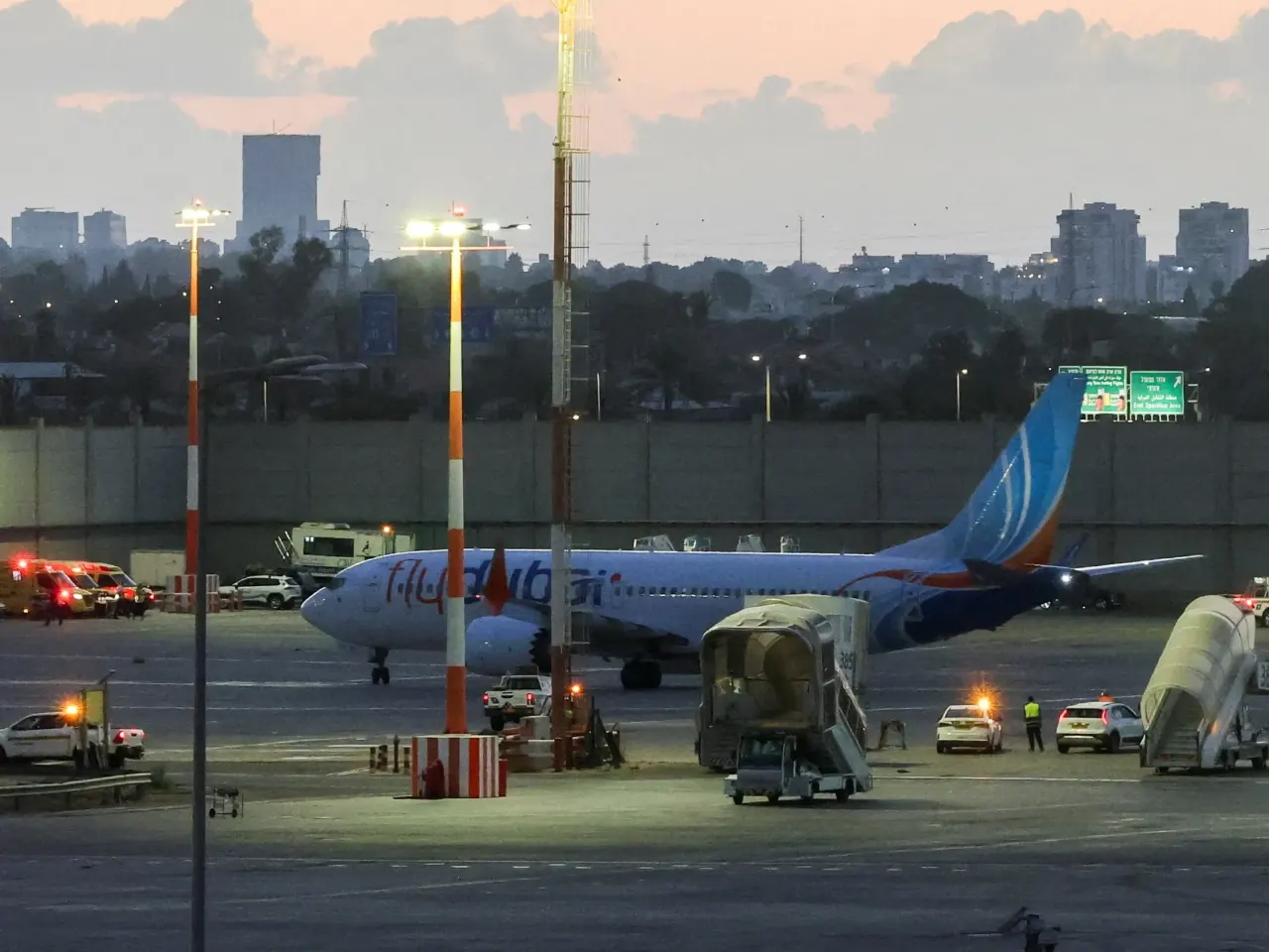 Flydubai airliner parked on airport apron at dusk with emergency vehicles nearby.