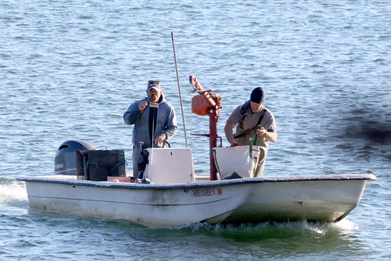 Two men work on a white boat with an outboard motor and lobster traps on open water.