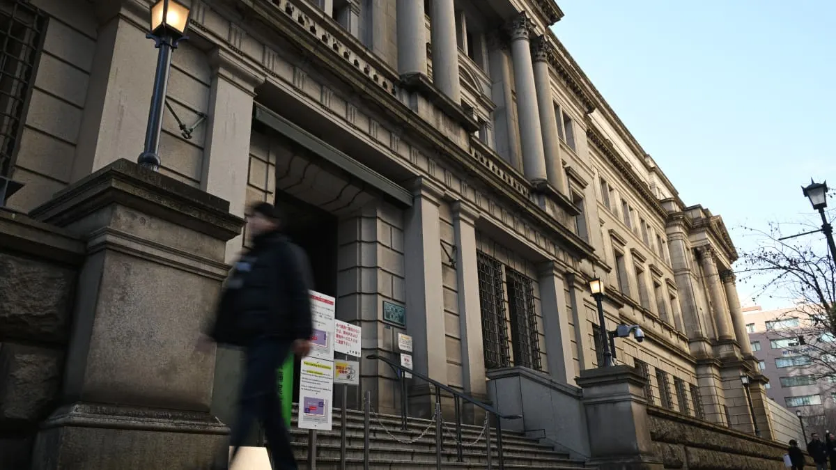 Exterior of a stone neoclassical bank building with a blurred pedestrian walking past the entrance.