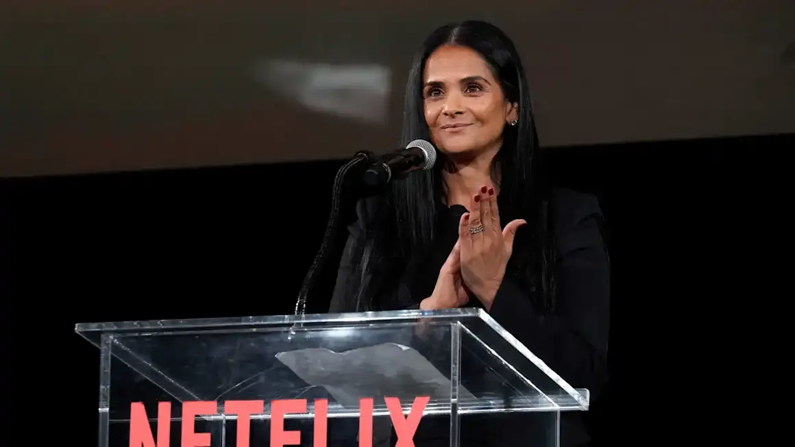 Smiling woman with long dark hair speaking at a clear podium with Netflix logo