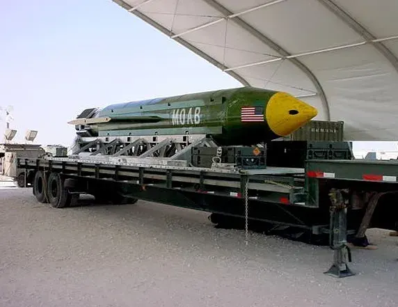 Massive GBU-43 MOAB bomb with yellow nose on flatbed trailer under a tent canopy.