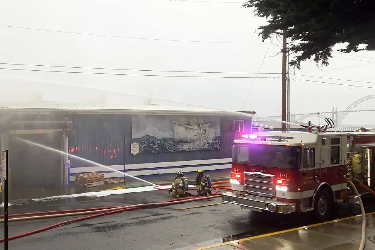 Firefighters spray water at a smoky building beside a Newport fire engine with lights flashing