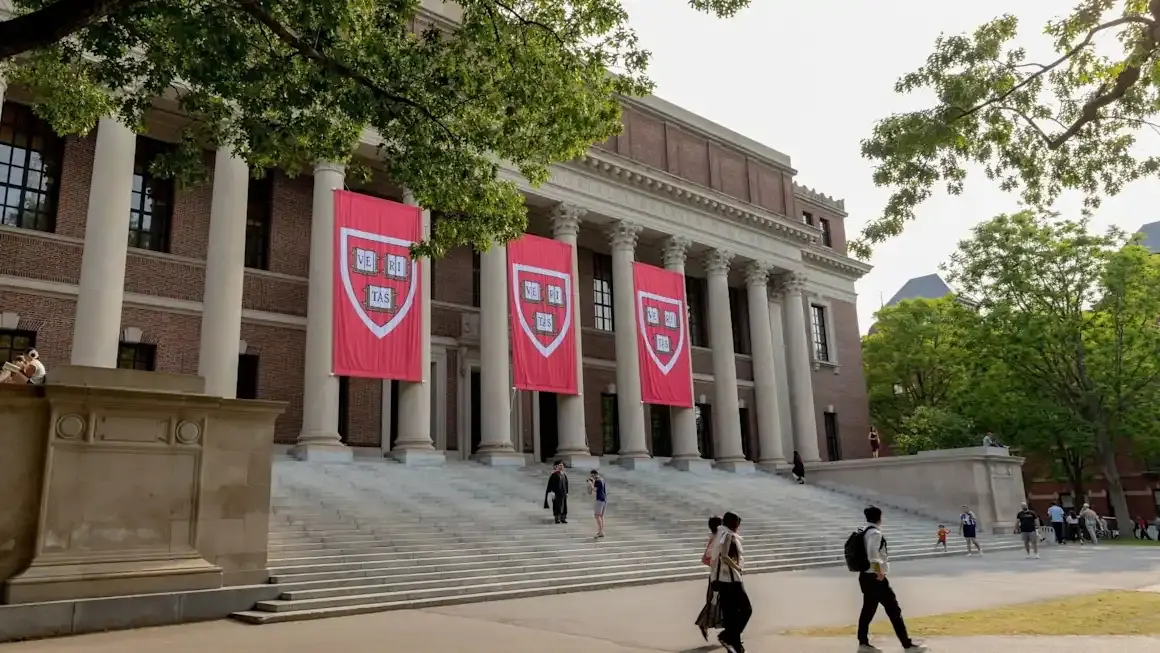 Harvard University columned building with crimson banners bearing university shield, students walking.