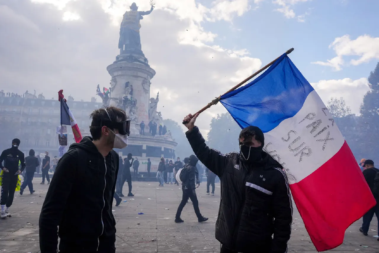 Masked protesters in a smoky Paris square, one waving a tricolour flag, statue in background.