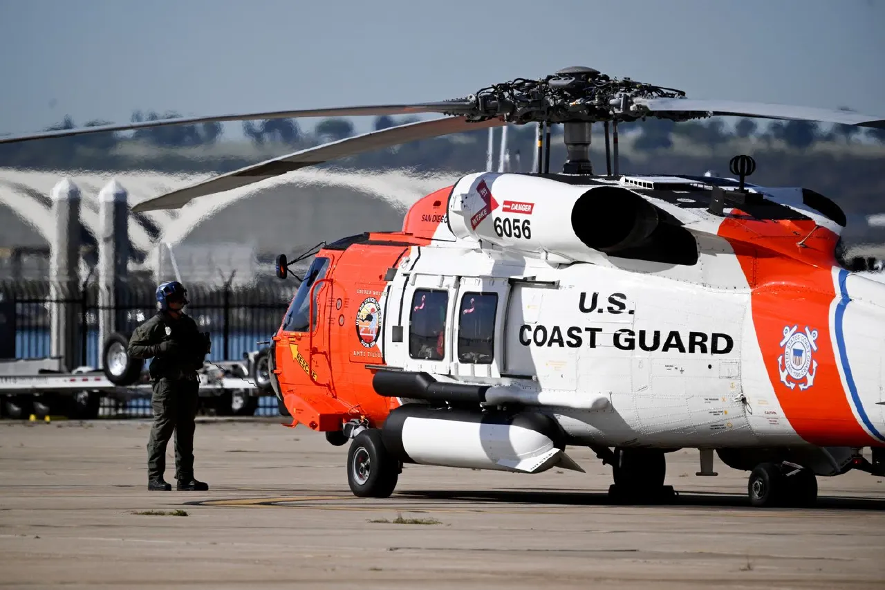 U.S. Coast Guard orange-and-white helicopter on tarmac with uniformed officer standing nearby
