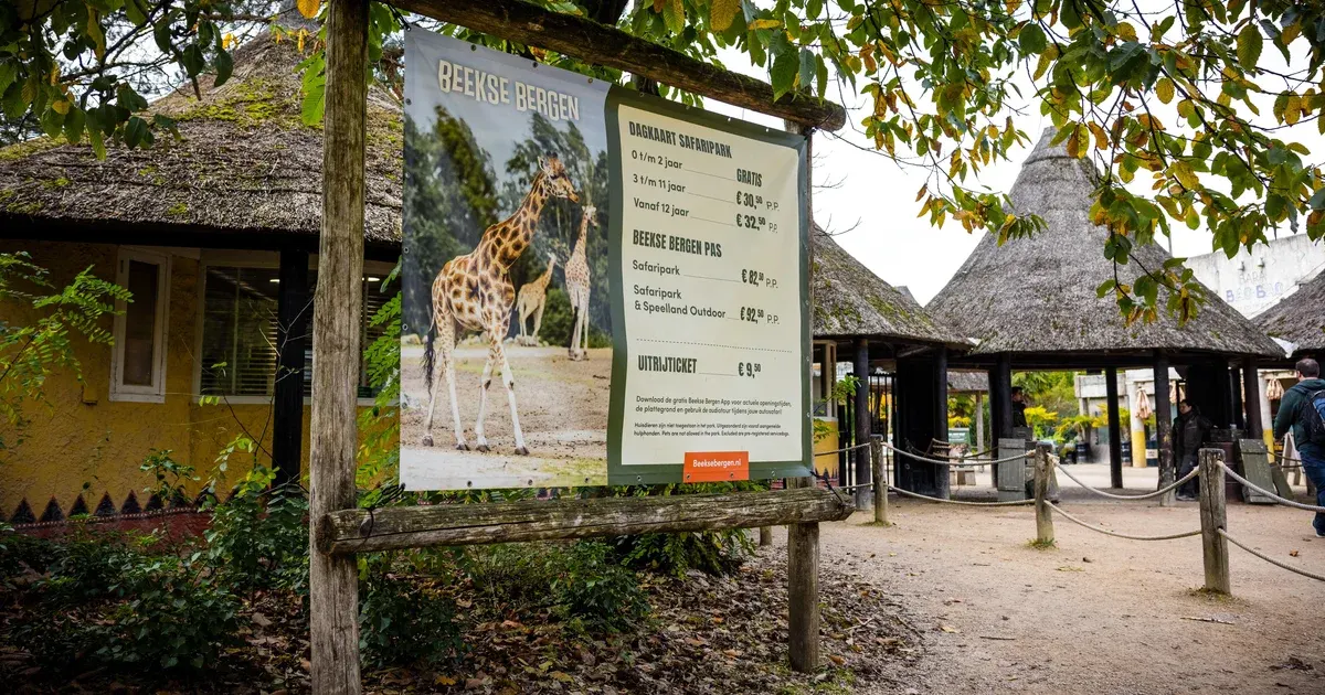 Beekse Bergen park entrance sign with giraffe photo and ticket prices, thatched buildings, visitors in background.