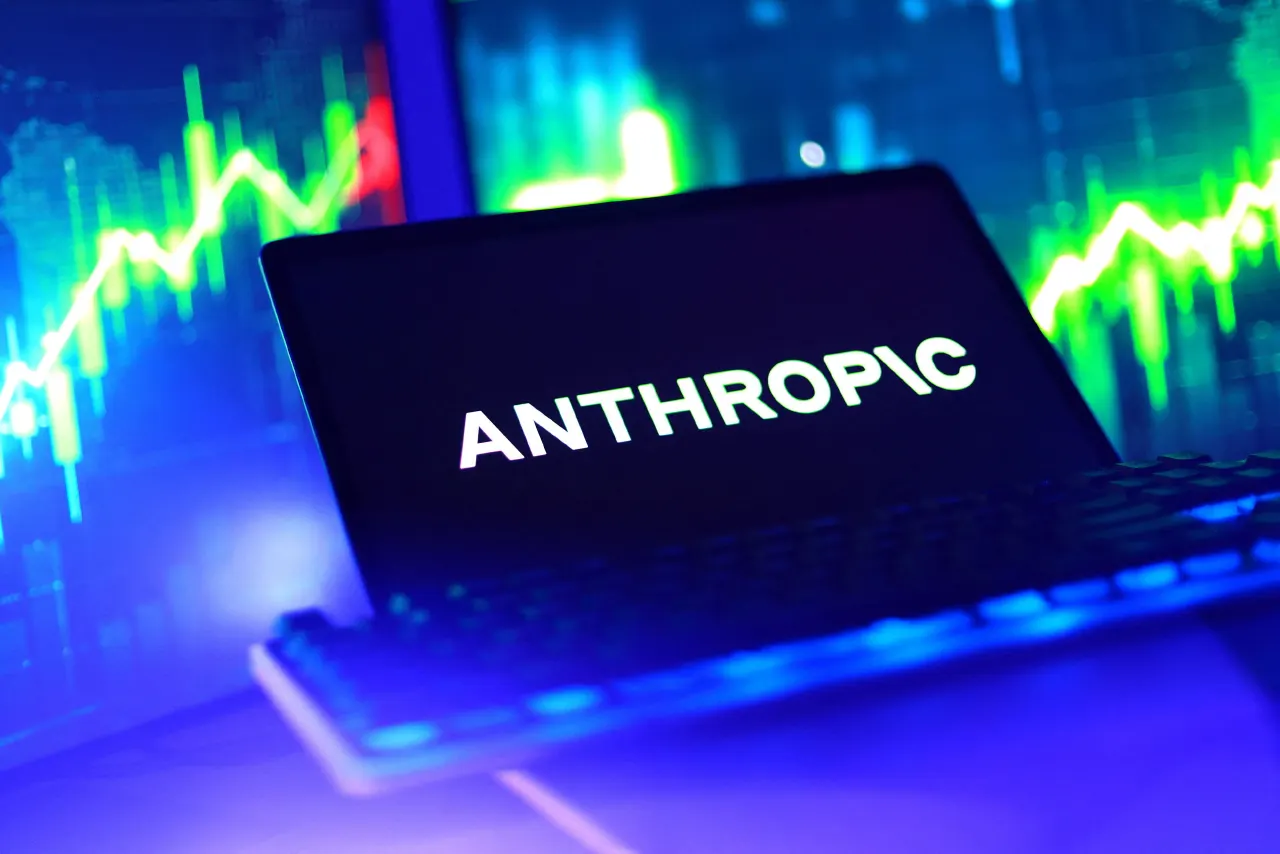 Laptop screen displaying Anthropic logo in front of glowing blue stock market charts