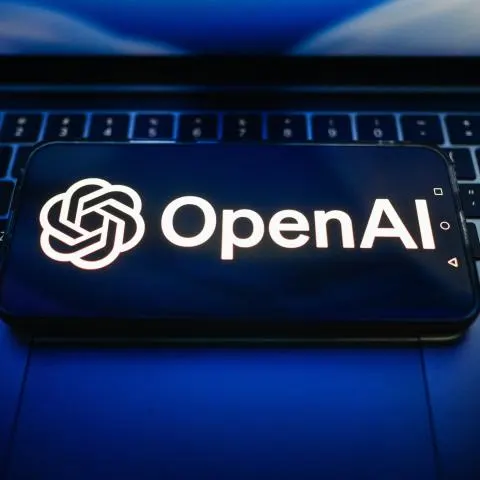 Smartphone screen displaying the OpenAI logo resting on a dark laptop keyboard.