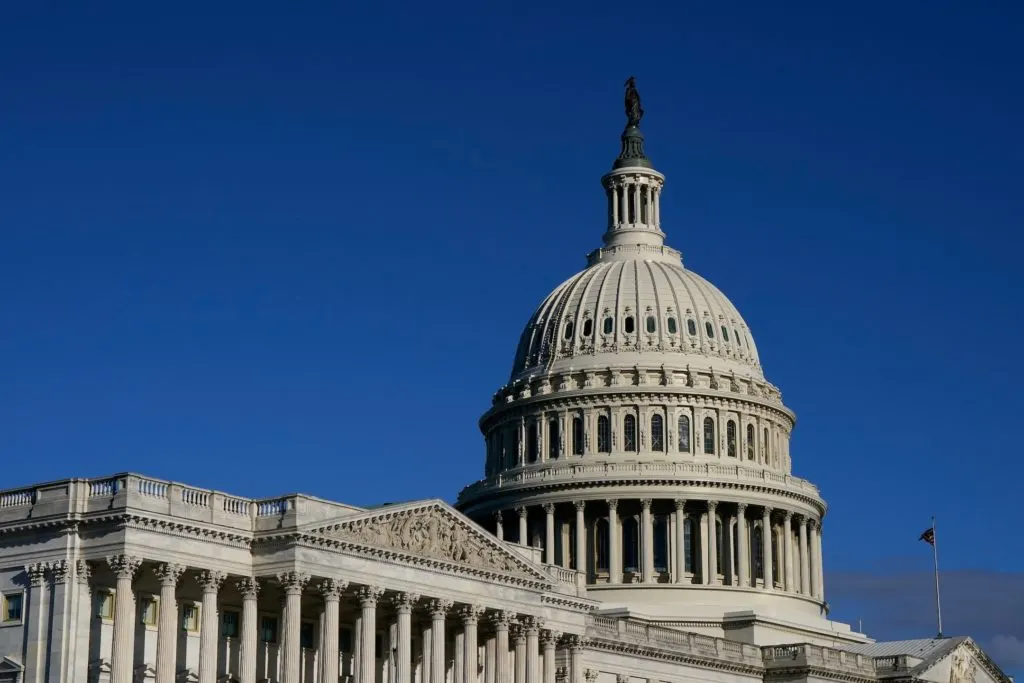 The U.S. Capitol dome and colonnaded facade against a clear blue sky