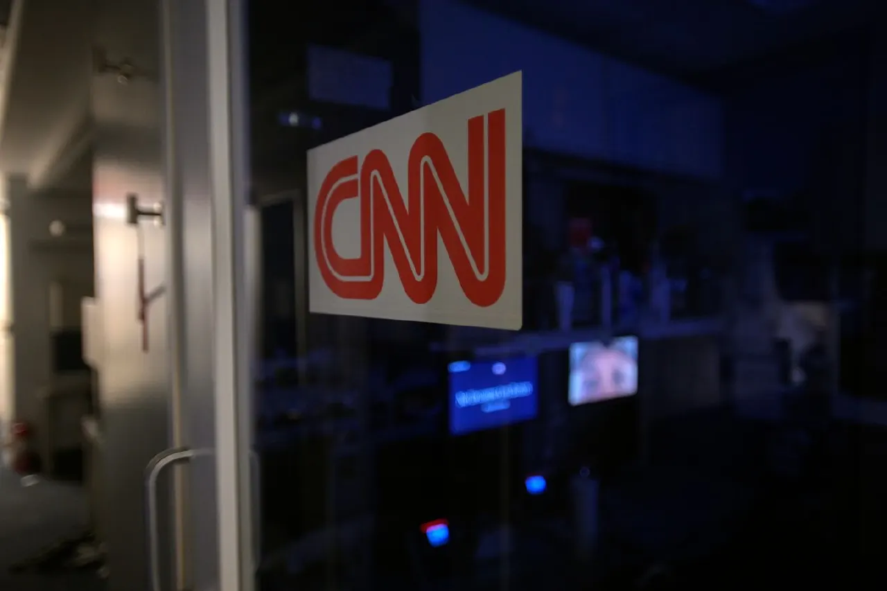 Red CNN logo on a glass door in a dimly lit newsroom interior