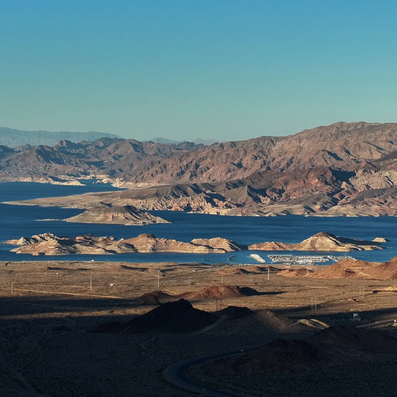 Wide view of Lake Mead surrounded by arid desert mountains and a marina under clear sky.
