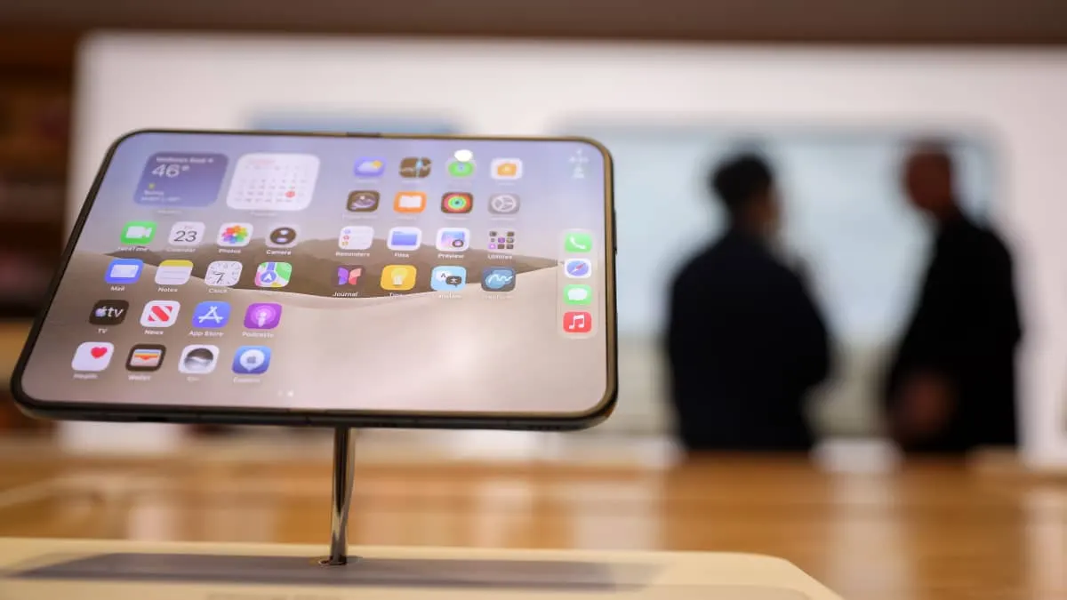 A smartphone with a home screen displayed on a stand in a store, with blurred people behind.
