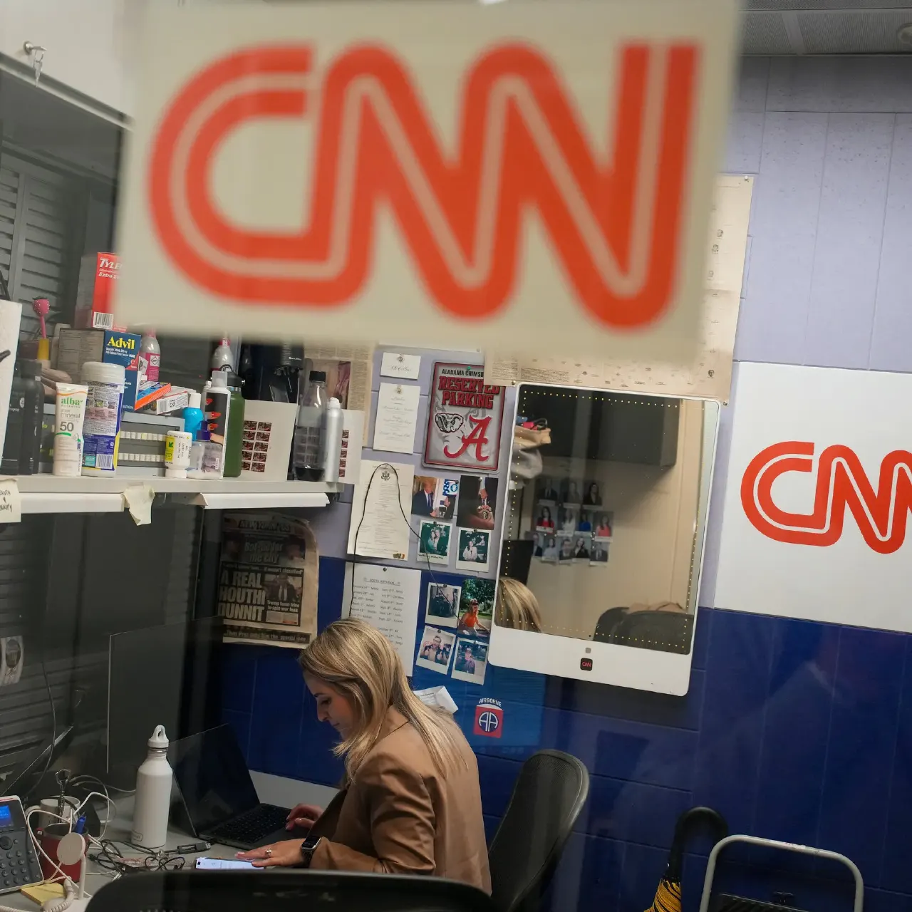 Woman working at a desk in a CNN-branded newsroom cubicle, with CNN logos visible.