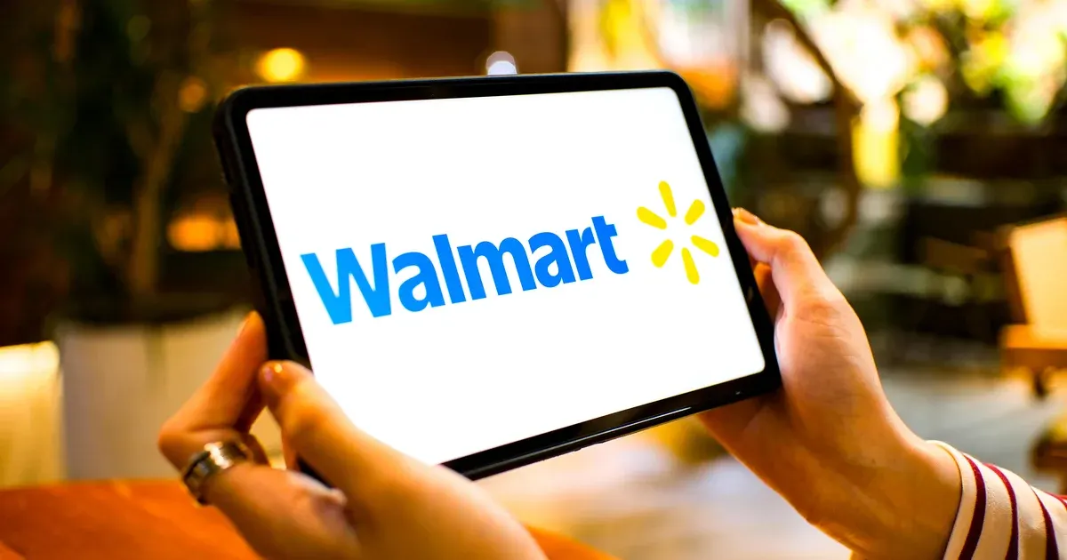 Hands hold a tablet showing the Walmart logo in a warm cafe setting.