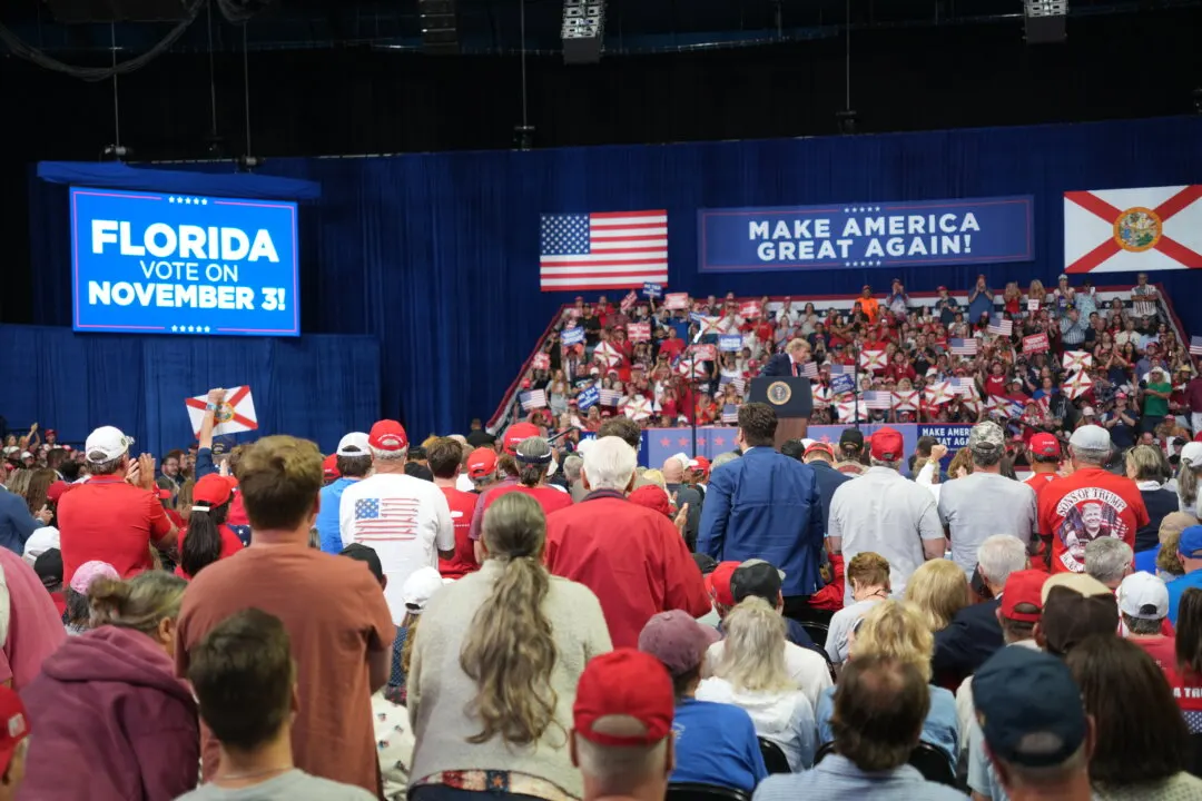 Large crowd in red caps and shirts at an indoor rally with US and Florida flags and signs
