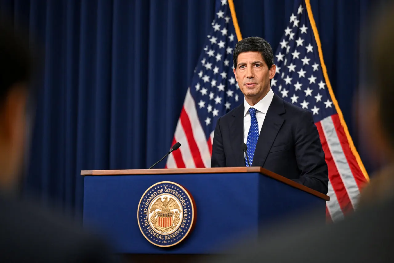 Man in dark suit speaking at podium with Federal Reserve seal, flanked by US flags