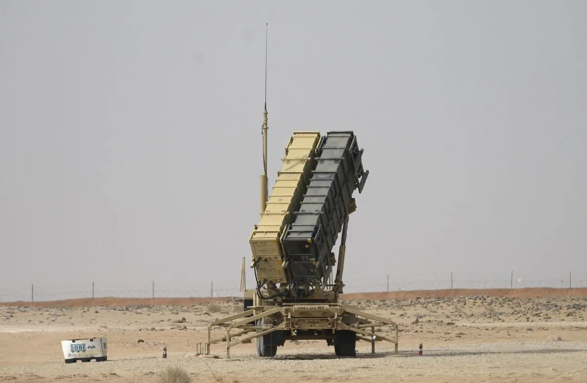 Tan air defense missile launcher vehicle on desert ground under hazy sky, with a small white cart nearby.