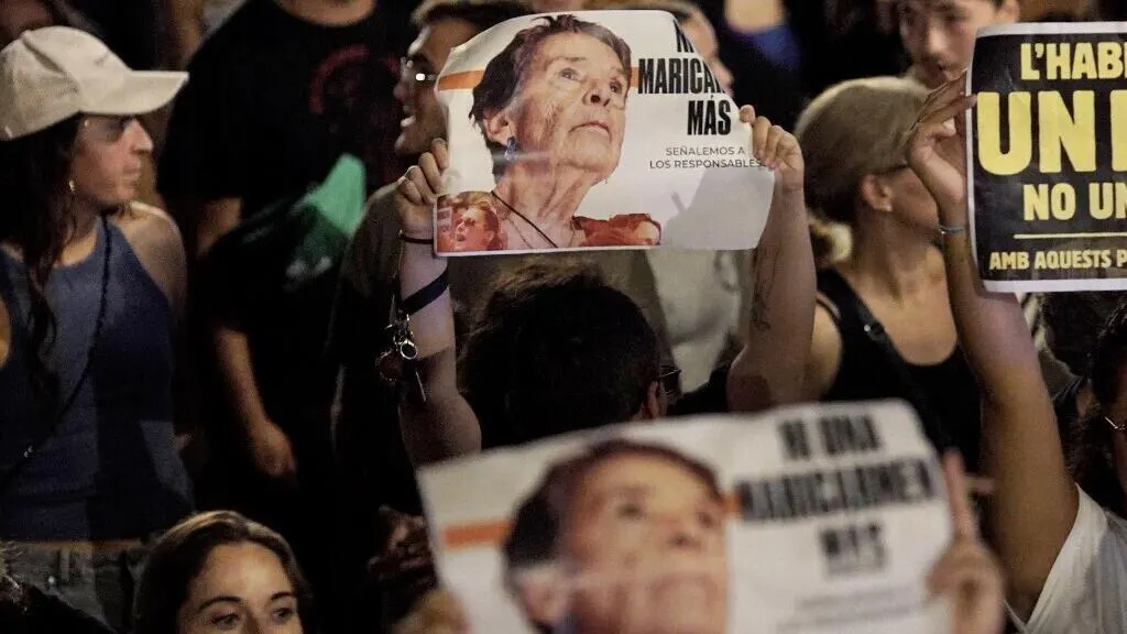 Crowd at night holding protest placards bearing a elderly woman's photo and slogan text.
