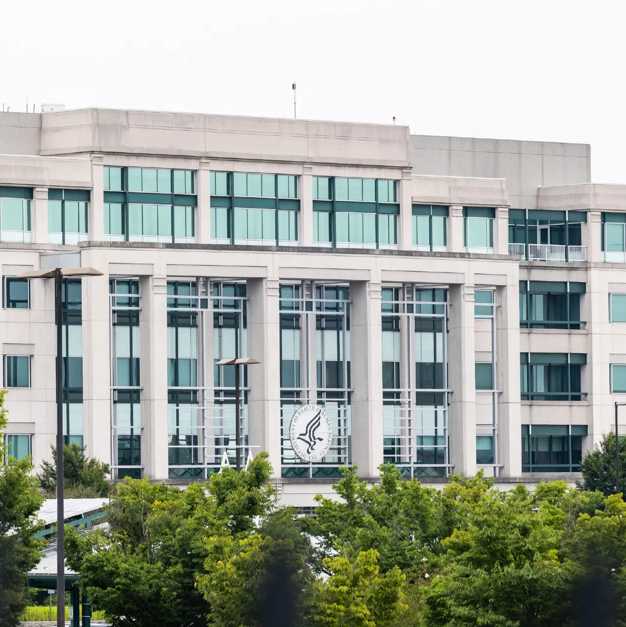 Large government office building facade with an agency seal on the glass, trees in foreground.