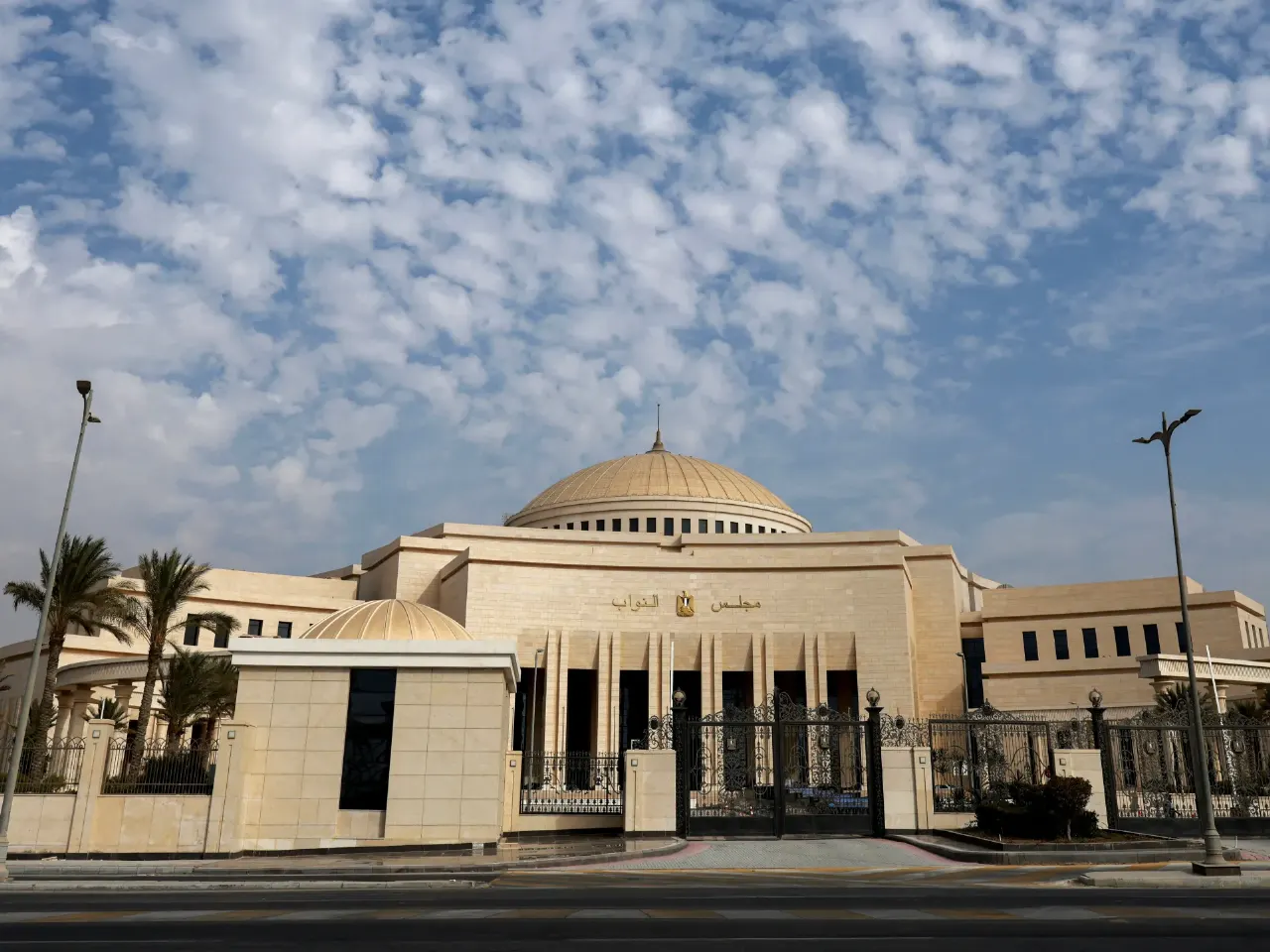 Domed cream-colored parliament building with Arabic script over entrance, black iron gates, blue sky