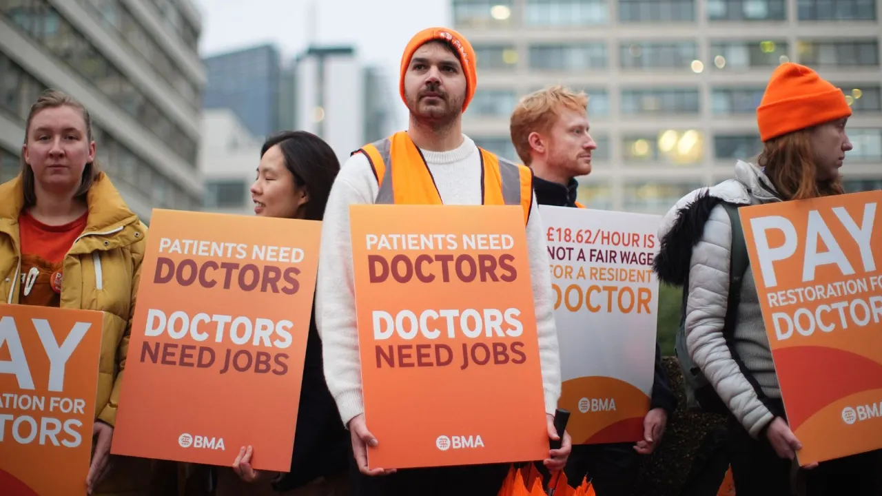 Striking doctors holding orange BMA placards reading 'Patients need doctors, doctors need jobs' outdoors.