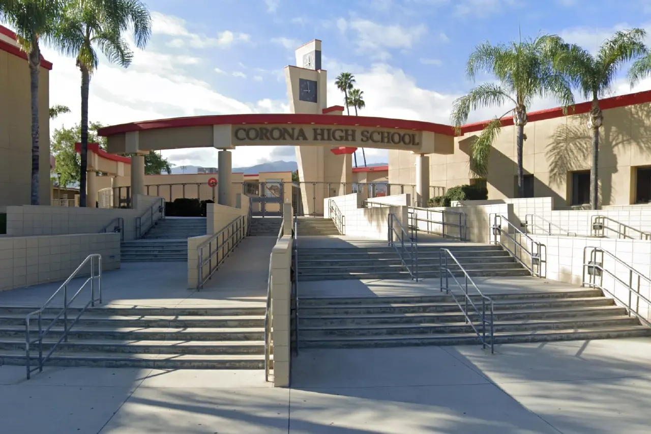 Entrance archway and steps of Corona High School with palm trees under blue sky