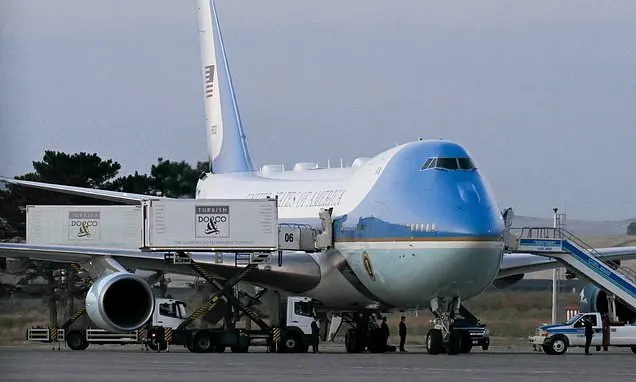 Large blue-and-white presidential-style jet parked on tarmac with cargo loader and stairs.
