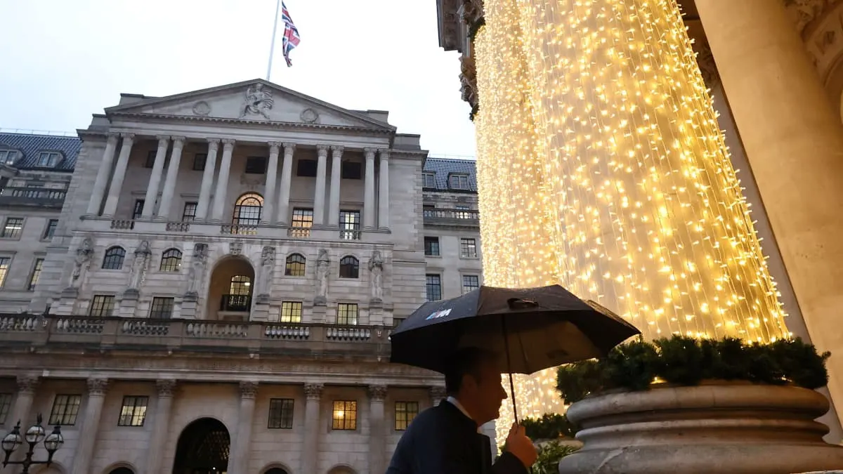 Bank of England building with Union Jack and person under umbrella beside festive fairy lights