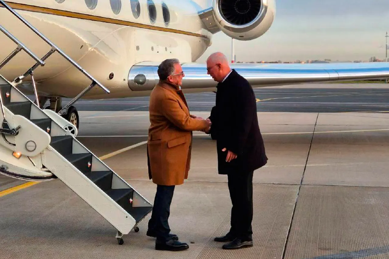 Two men shake hands beside a white private jet on an airport tarmac at dusk.