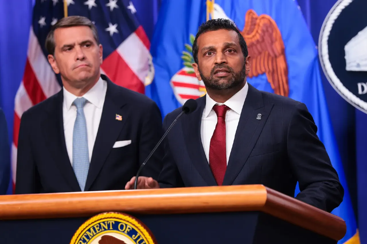 Two men in dark suits at a podium before US flags and the Department of Justice seal.
