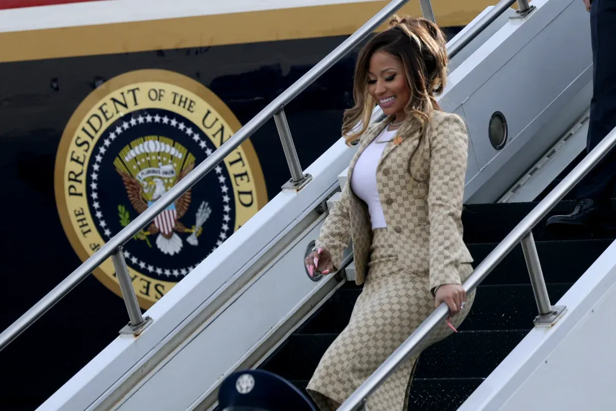 Smiling woman in checkered beige suit descending aircraft stairs, with presidential seal on fuselage.