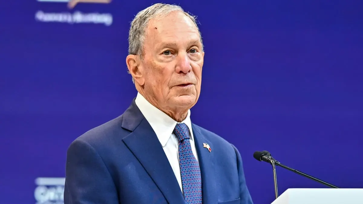 Older man in navy suit speaks at a podium before a blue backdrop.