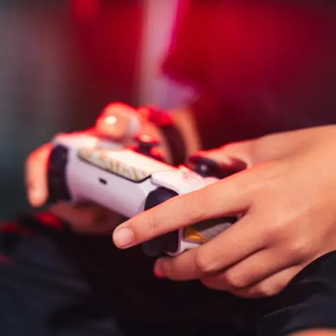 Close-up of hands holding a white game controller under red ambient light.