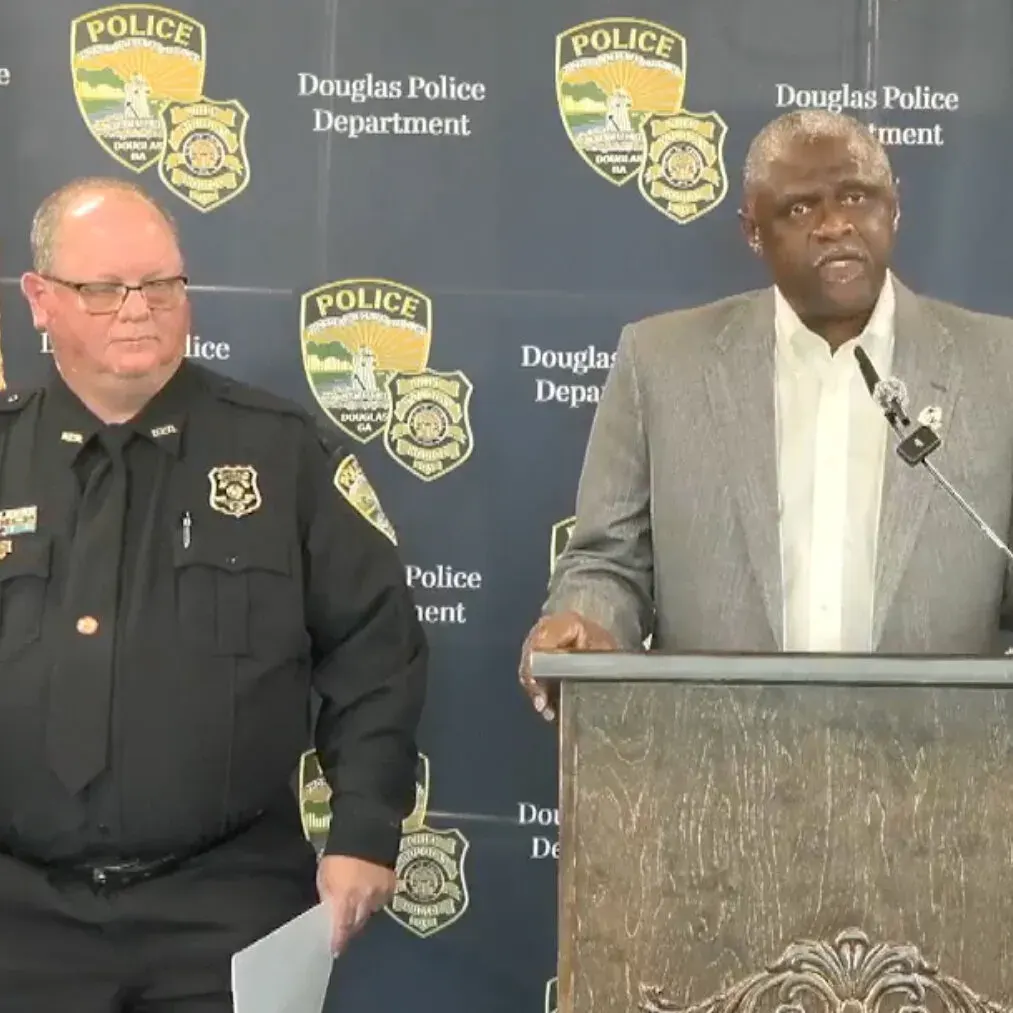 Two men at a press conference before Douglas Police Department backdrop, one speaking at a podium.