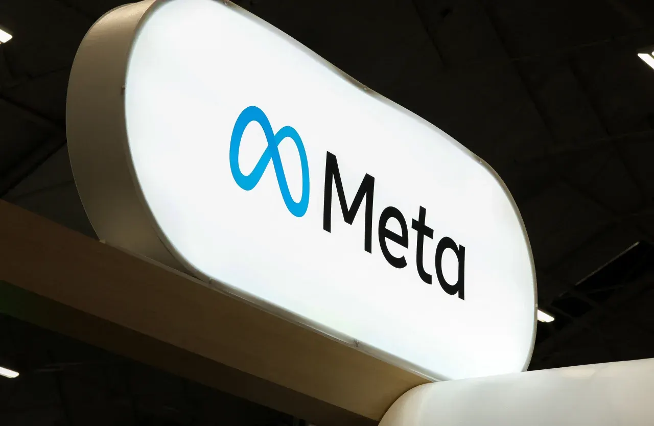 Illuminated Meta logo sign mounted overhead, photographed from below against a dark ceiling.