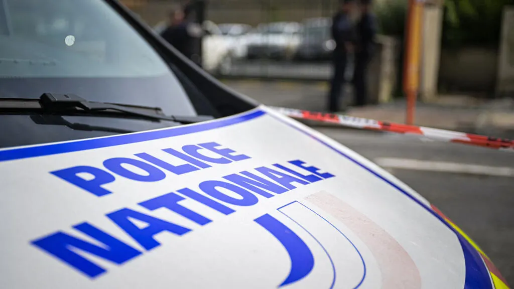 Close-up of a French Police Nationale vehicle bonnet, with police tape and officers in the blurred background.