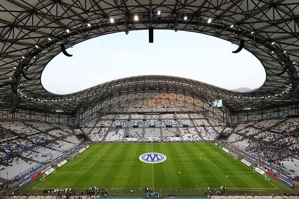 Wide view of a covered stadium with a central circle logo and mostly empty stands.