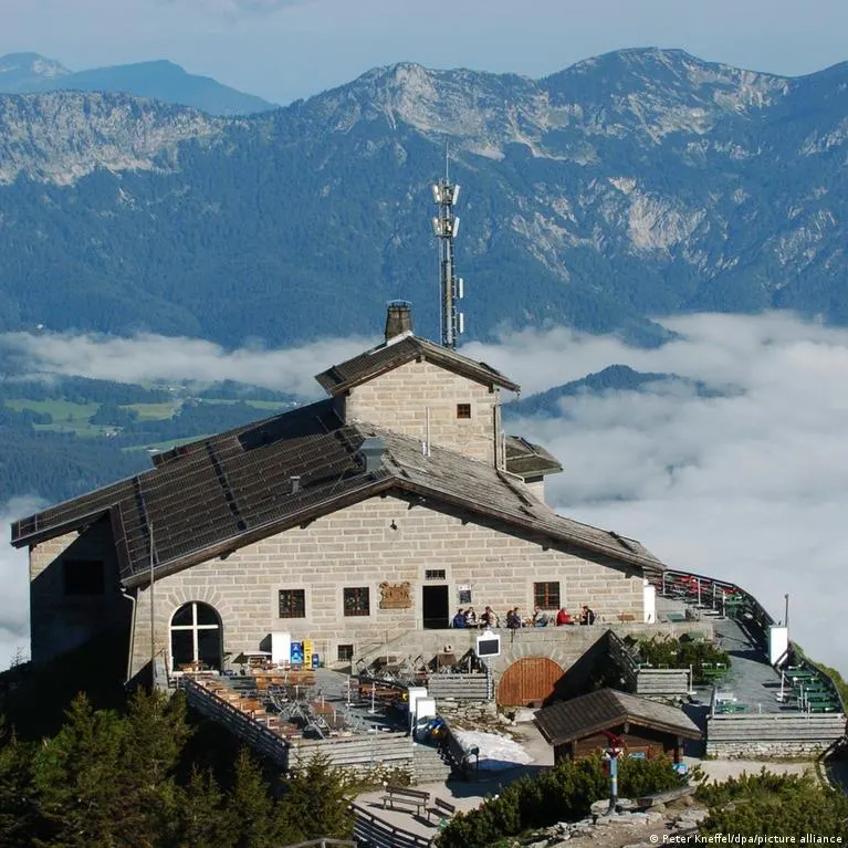Stone Eagle's Nest mountain house on a peak above clouds, with visitors on the terrace.