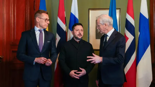 Three men in suits talking in a room in front of several national flags.