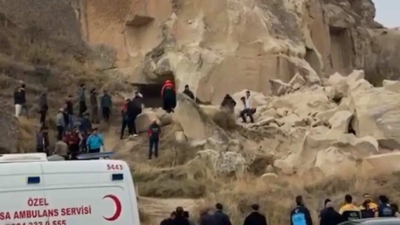 Rescuers and onlookers gather at fallen rock debris beside an ambulance at a cliff site.