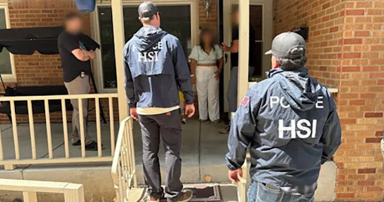 Two agents in HSI jackets stand at a front porch while residents, faces blurred, stand in the doorway.