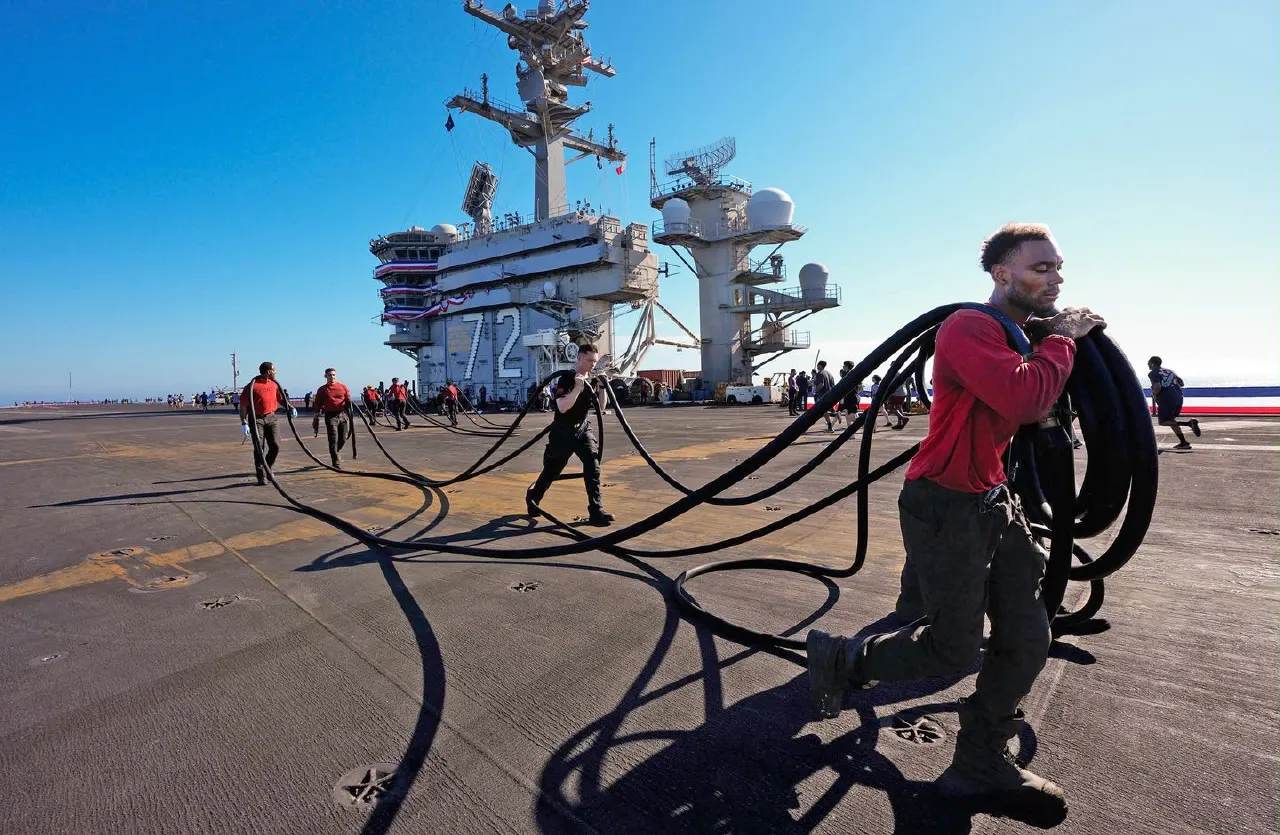 Sailors in red shirts hauling black cables across a carrier flight deck near the ship's island tower.