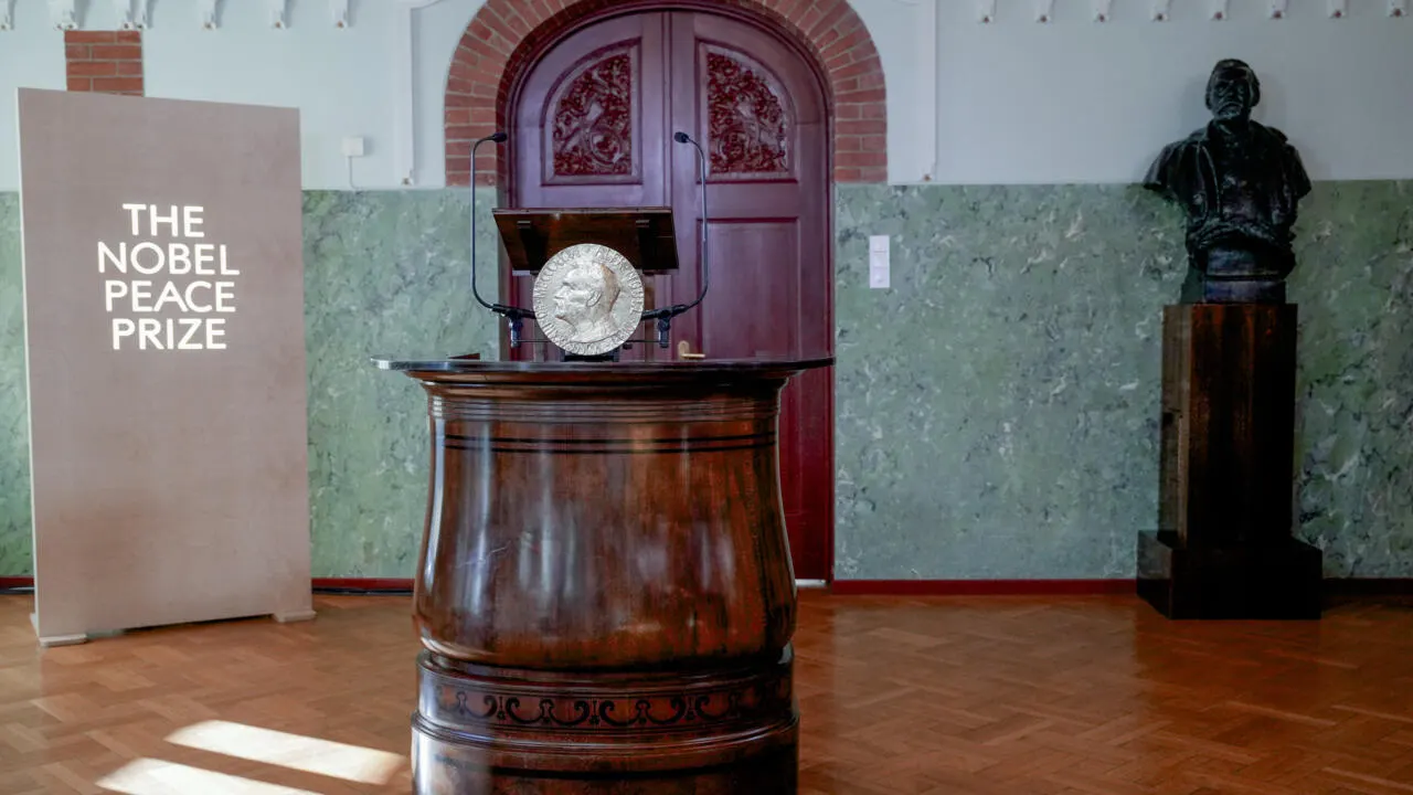Nobel Peace Prize medal displayed on a wooden podium in an ornate room, with a bust nearby.