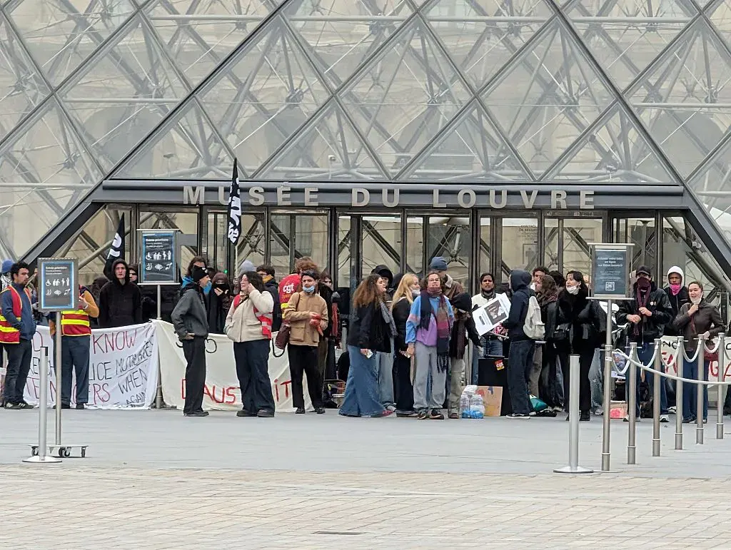 Crowd of protesters with banners blocking entrance of Musée du Louvre pyramid in Paris.