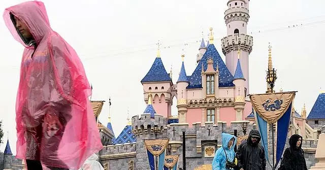 Rain-ponchoed guests walk before Sleeping Beauty Castle at Disneyland during rainy weather.