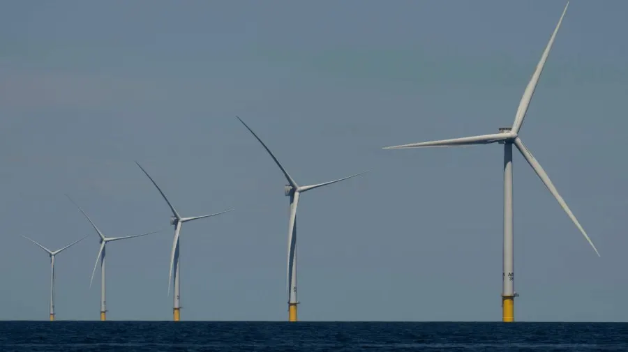 Row of offshore wind turbines with yellow bases rising from calm blue sea under hazy sky.