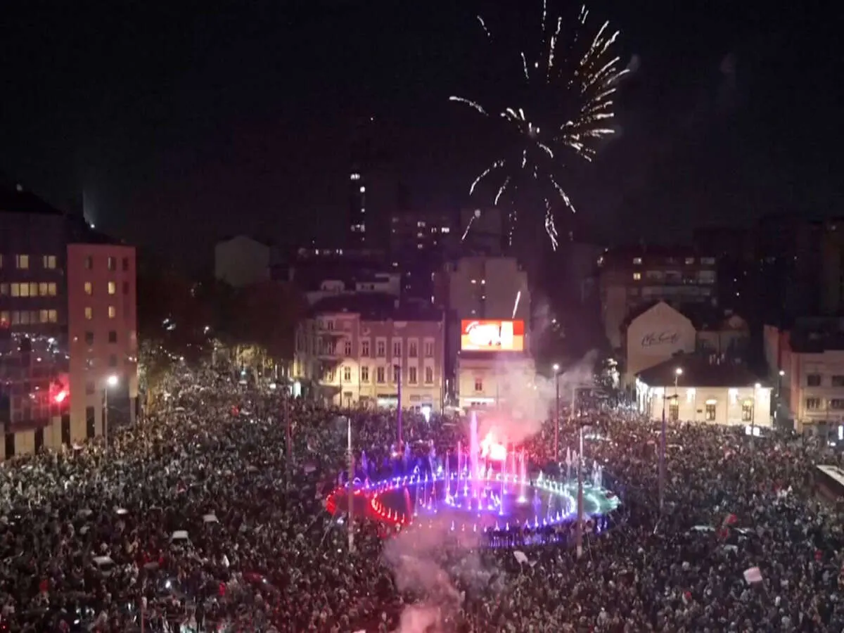 Huge night crowd celebrating in city square with fireworks, fountain lights and smoke