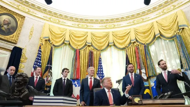 Men in suits stand around a seated man gesturing in the ornate gold-draped Oval Office.