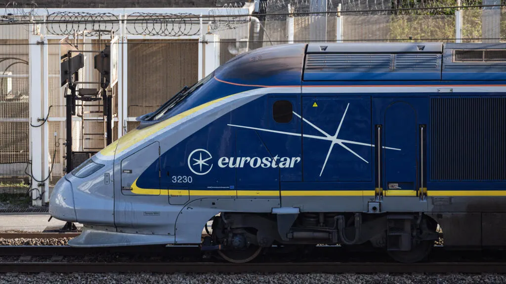 Eurostar high-speed train with blue livery and wire fencing, at a rail platform.